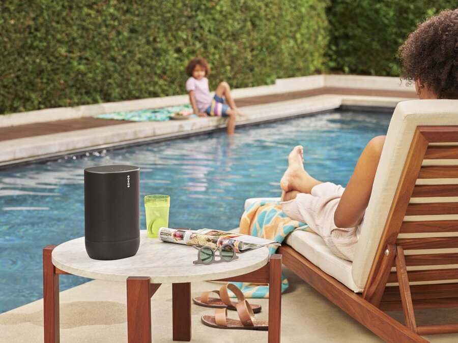 A woman sitting poolside with a Sonos outdoor speaker next to her on a side table.